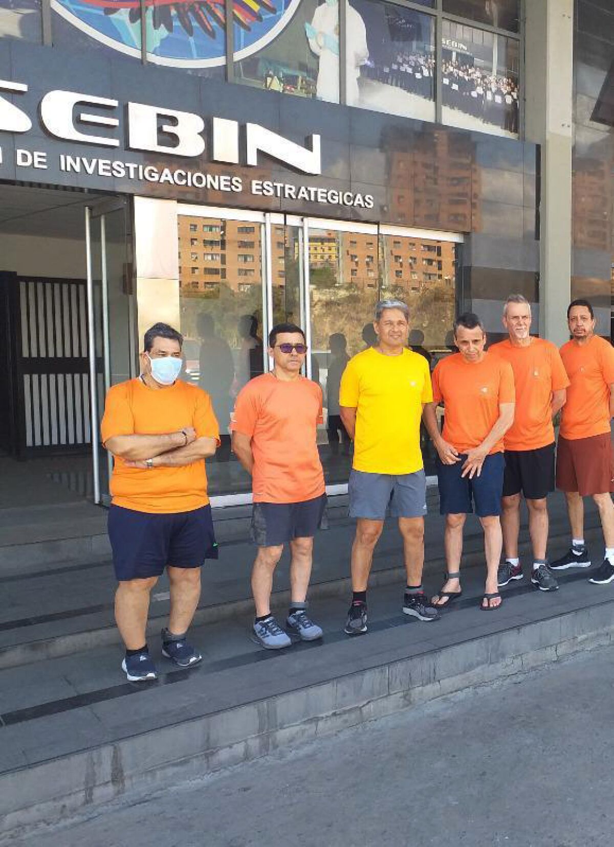 Six people in T-shirts and shorts stand outside a building.