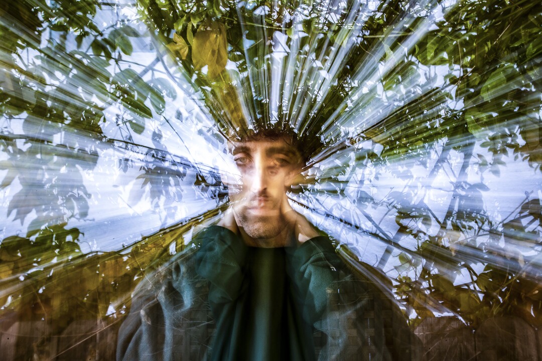 Sam Gendel in a stylized photo with beams of light and leaves spreading out around him
