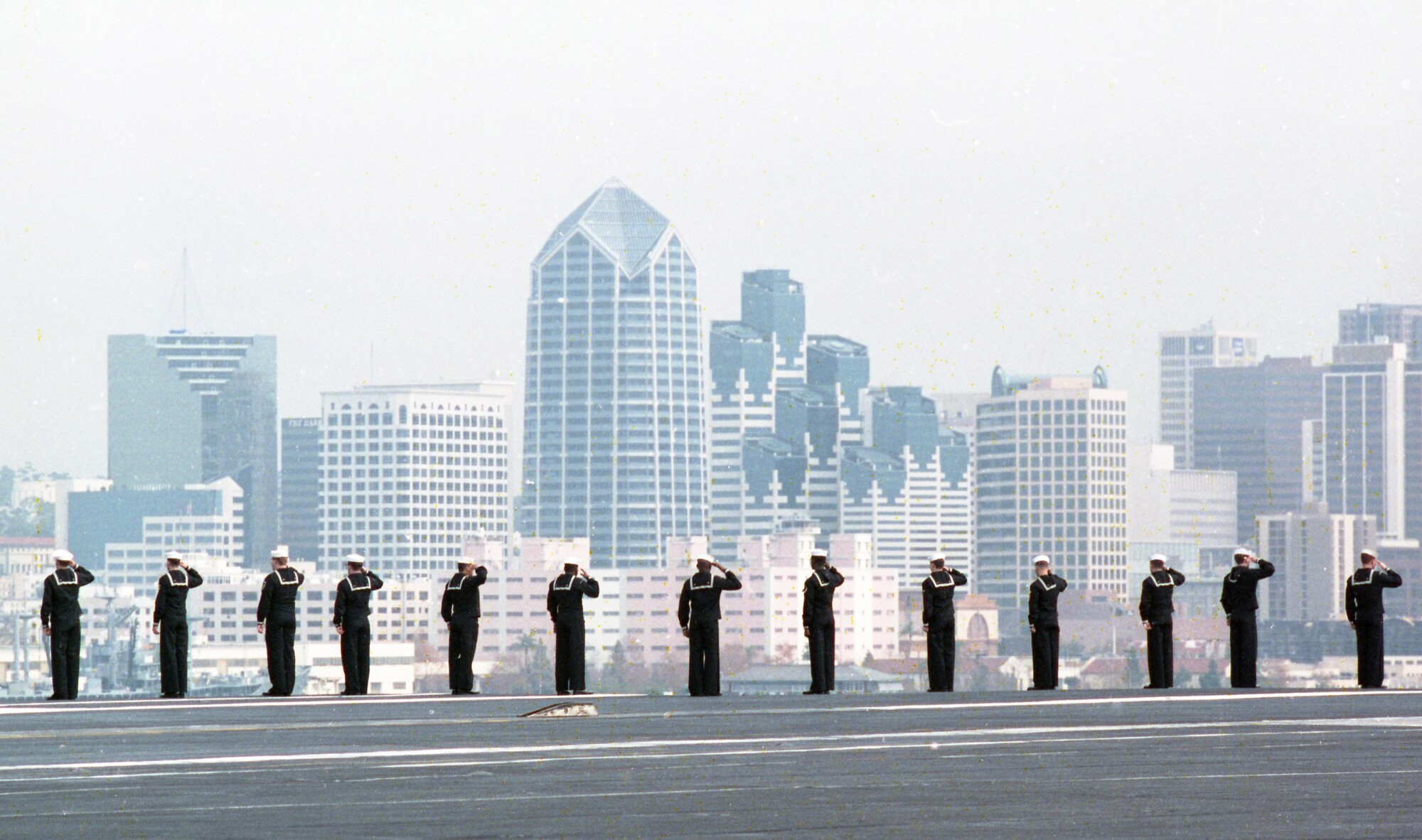 With the city skyline in the background sailors aboard the aircraft carrier Kitty Hawk line flight deck