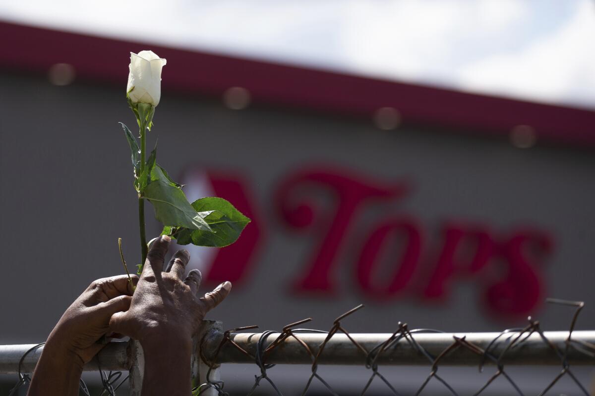 Cariol Horne, 54, places a rose on the fence outside the Tops Friendly Market on Thursday, July 14, 2022, in Buffalo, N.Y. The Buffalo supermarket where 10 Black people were killed by a white gunman is set to reopen its doors, two months after the racist attack. (AP Photo/Joshua Bessex)