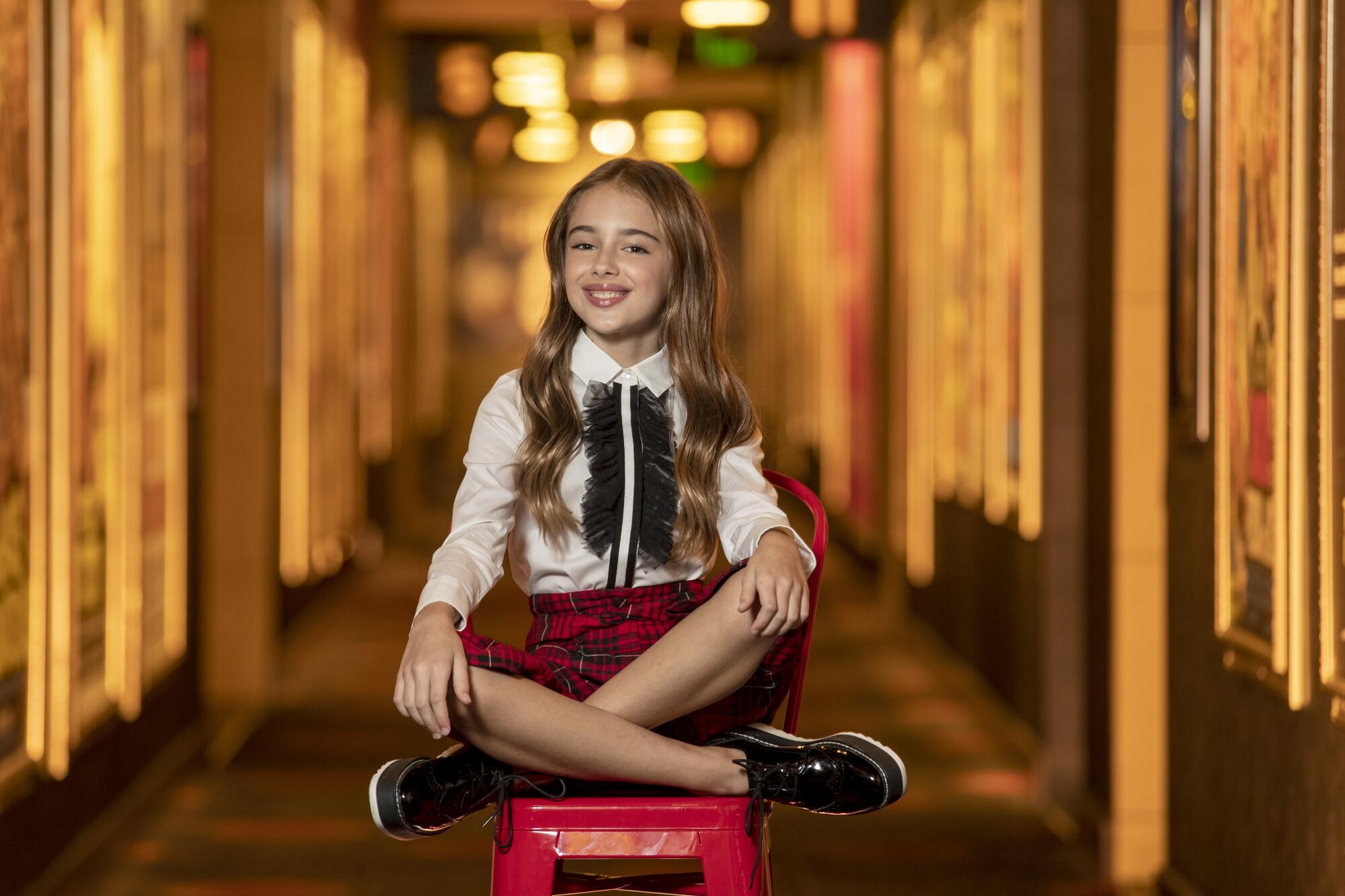 Julia Butters, 10, sitting cross-legged on a red chair.