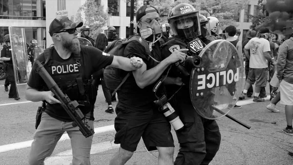 A black-and-white film still of a man battling two police in riot gear