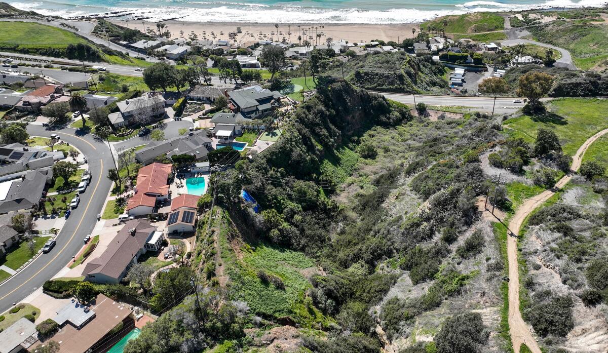 Aerial view of homes near deep land drops with a beach and ocean in the background.