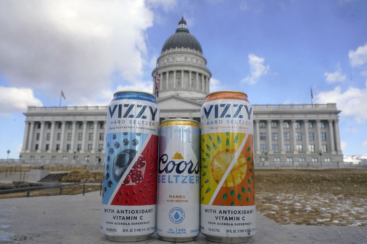 A can of Coors Seltzer Mango, center, is shown with Vizzy Blueberry Pomegranate, left, and Vizzy Pineapple Mango, in front of the Utah State Capitol, Thursday, Feb. 17, 2022, in Salt Lake City. A bill advancing at the Utah Legislature would remove nearly half of popular hard seltzer products from the shelves of grocery and convenience stores. At issue is a unique-to-Utah dustup over flavorings with trace amounts of alcohol. (AP Photo/Rick Bowmer)
