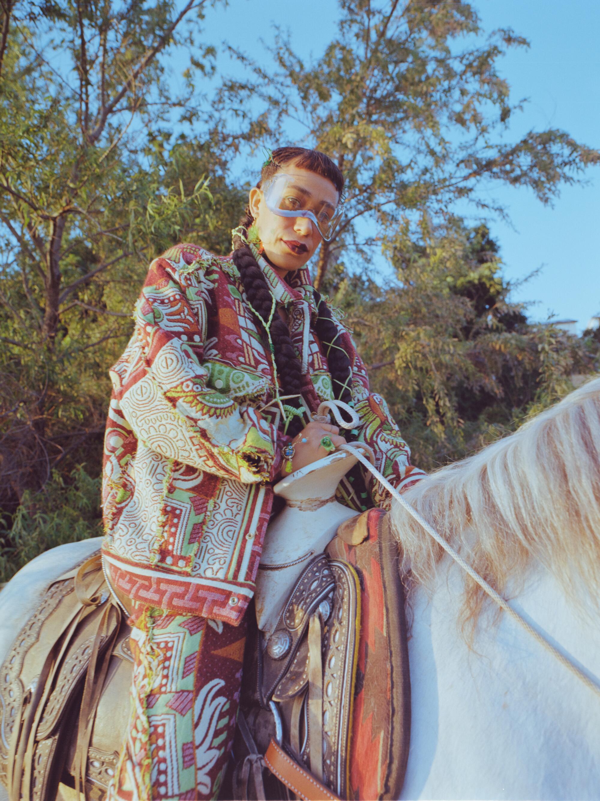 A model in a patterned outfit sits on a horse.