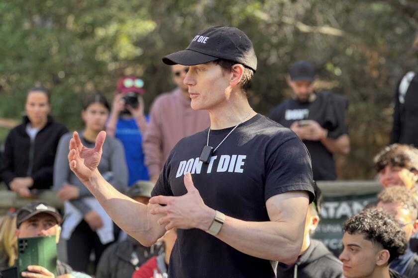 A man wearing a hat and shirt that read "Don't Die" speaks to a crowd