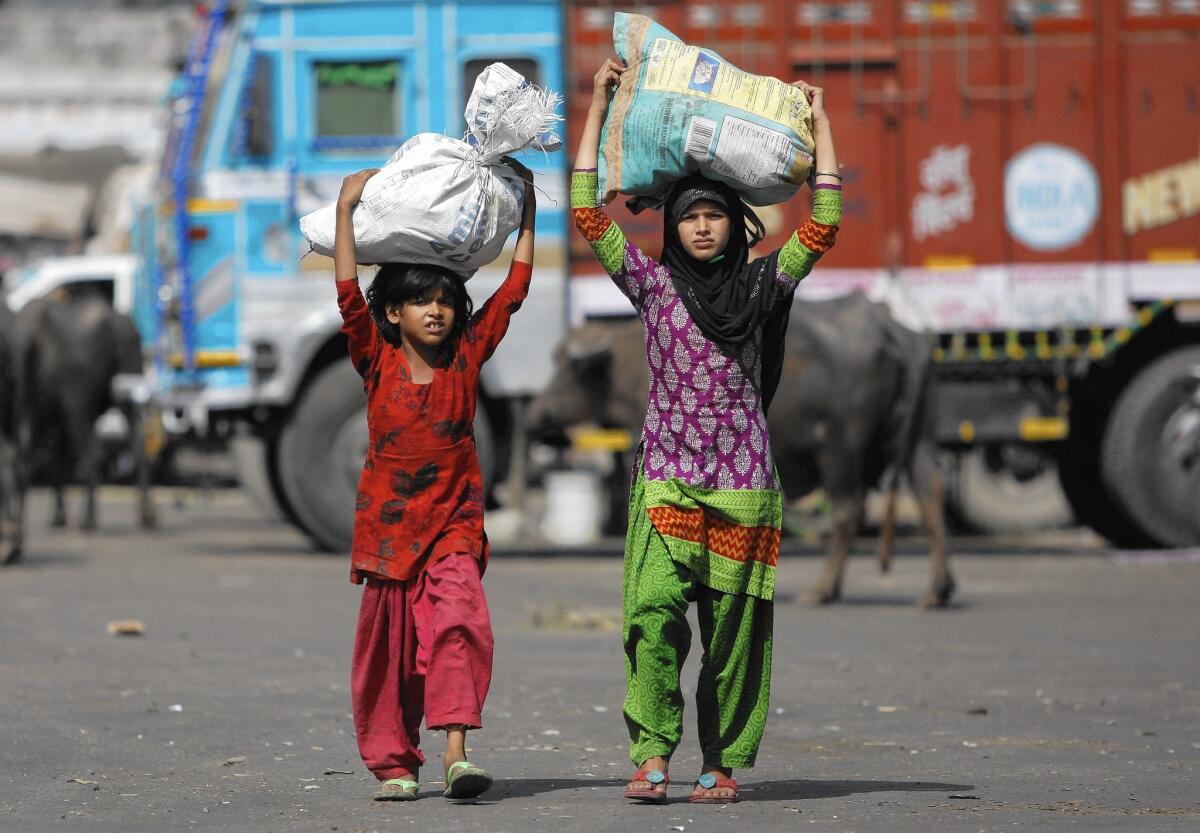 Children carry sacks of leftover vegetables collected from a wholesale market to be sold in their shantytown on June 12, 2015, on the outskirts of Jammu, India.