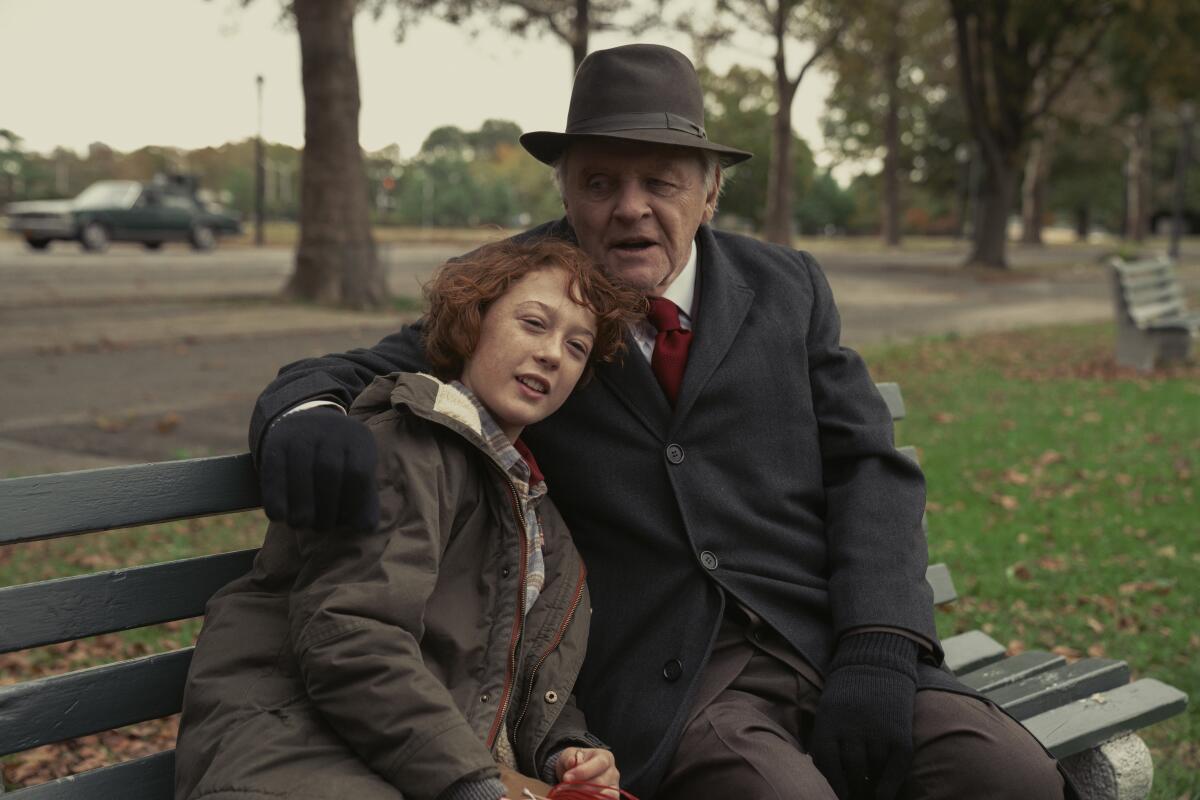 a boy leans against a man with his arm around him on a park bench 