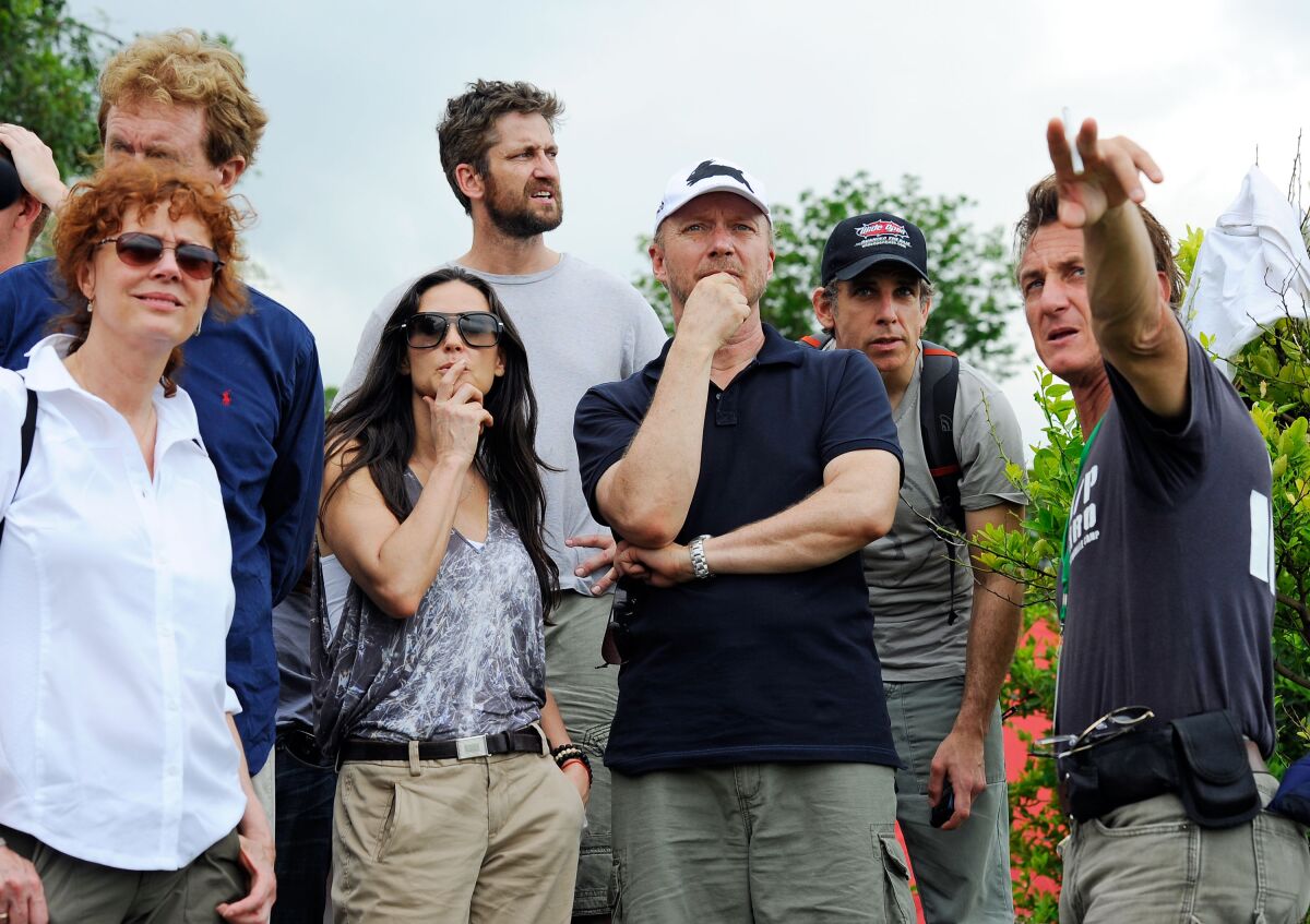 Seven men and women look on thoughtfully as another man points off into the distance