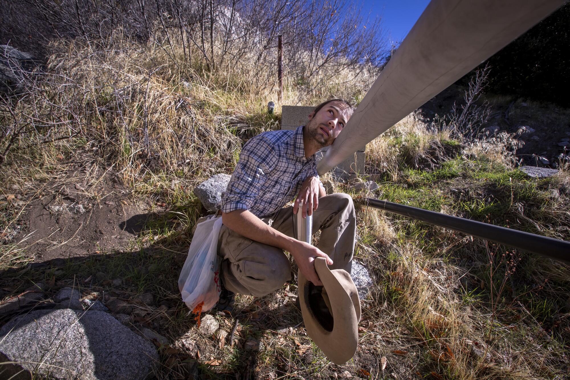 A man inspects a suspended pipeline on a hillside.