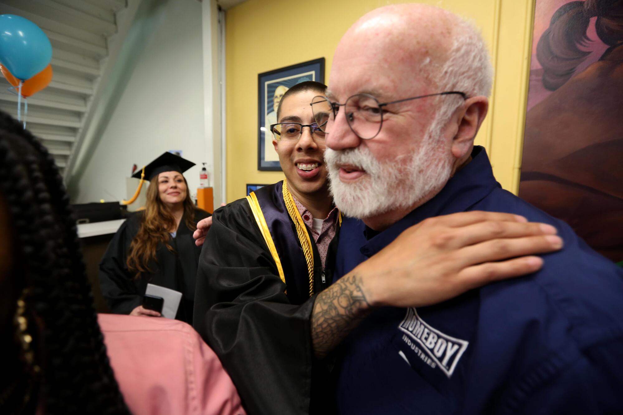 A young man in a graduation gown embraces an older man.