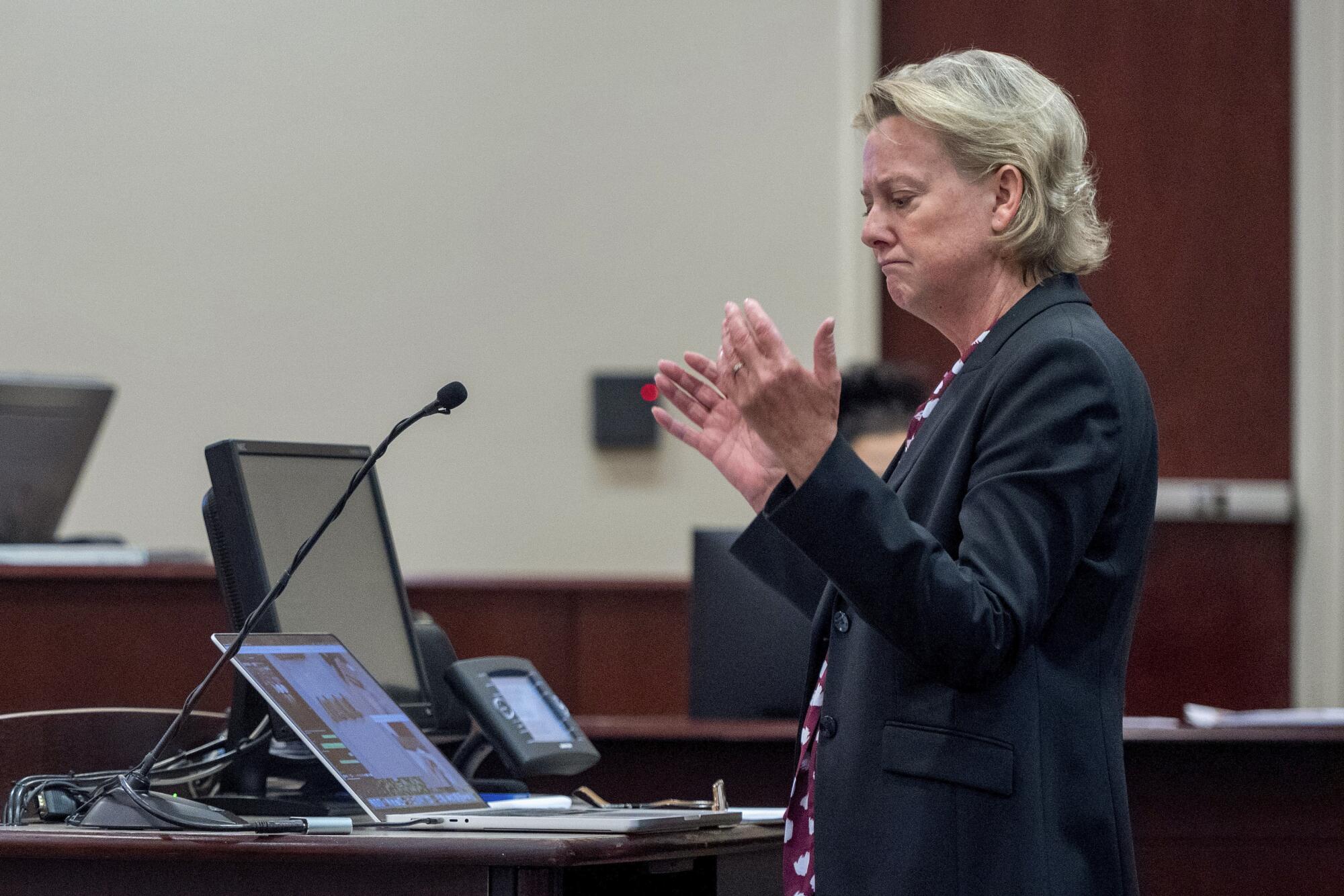 Special prosecutor Kari T. Morrissey holds out her hands while standing and looking at a laptop screen in court.