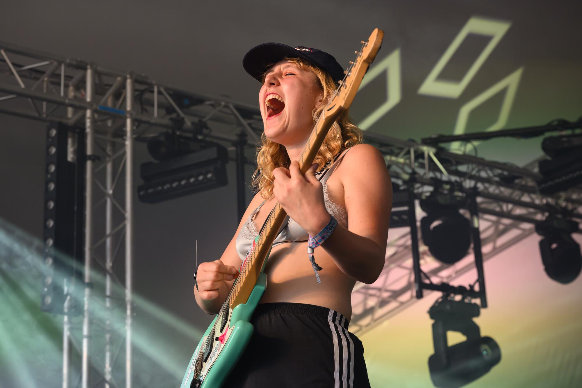 Phoebe Lunny of Lambrini Girls singing and playing electric guitar in a black ballcap and bikini top
