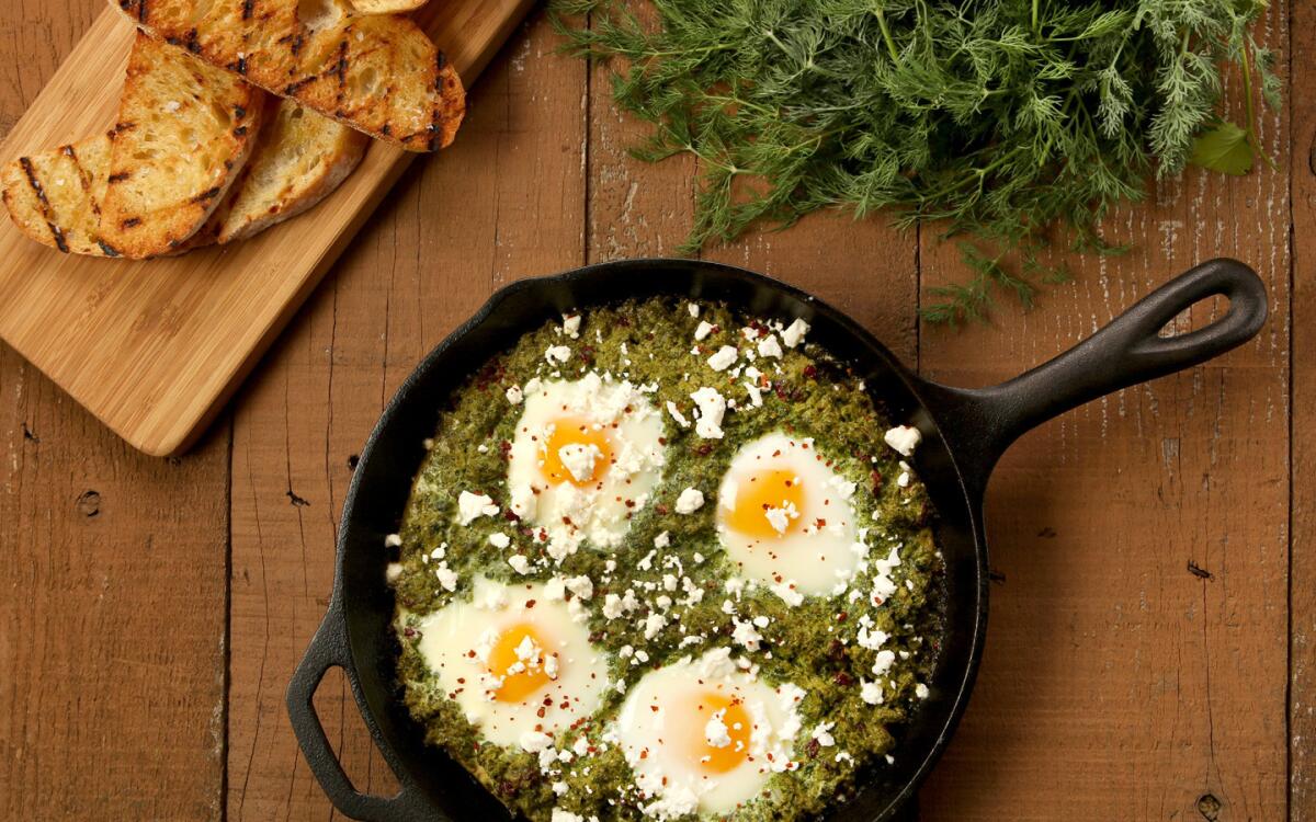 Deconstructed kuku sabzi in a skillet with grilled ciabatta bread on a wooden board beside it.