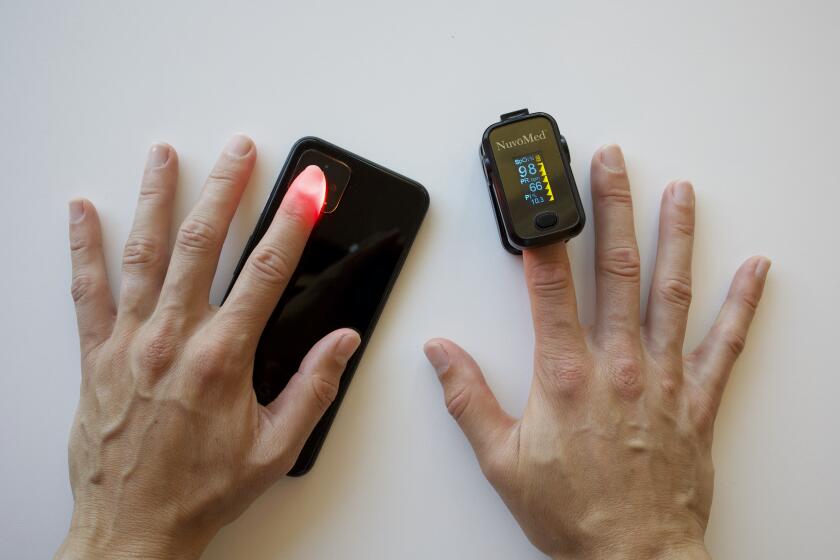 A participant simultaneously tests the new smartphone oximetry technique on their left finger and a standard pulse oximeter on their right finger.