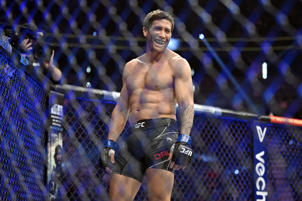 A shirtless man with a mouthguard laughing inside a fighting ring