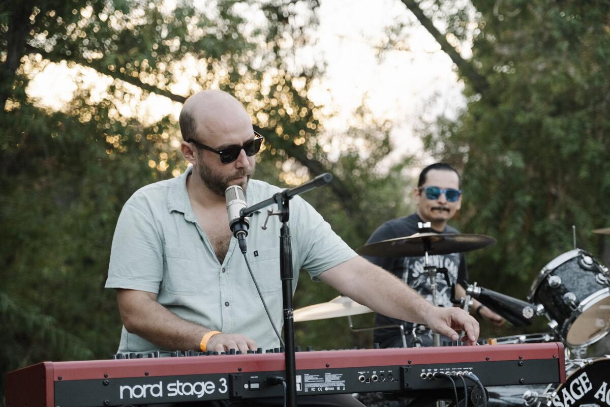 Sage Against the Machine co-founder Evan Meyer at his keyboard in an open-neck shirt and dark glasses.
