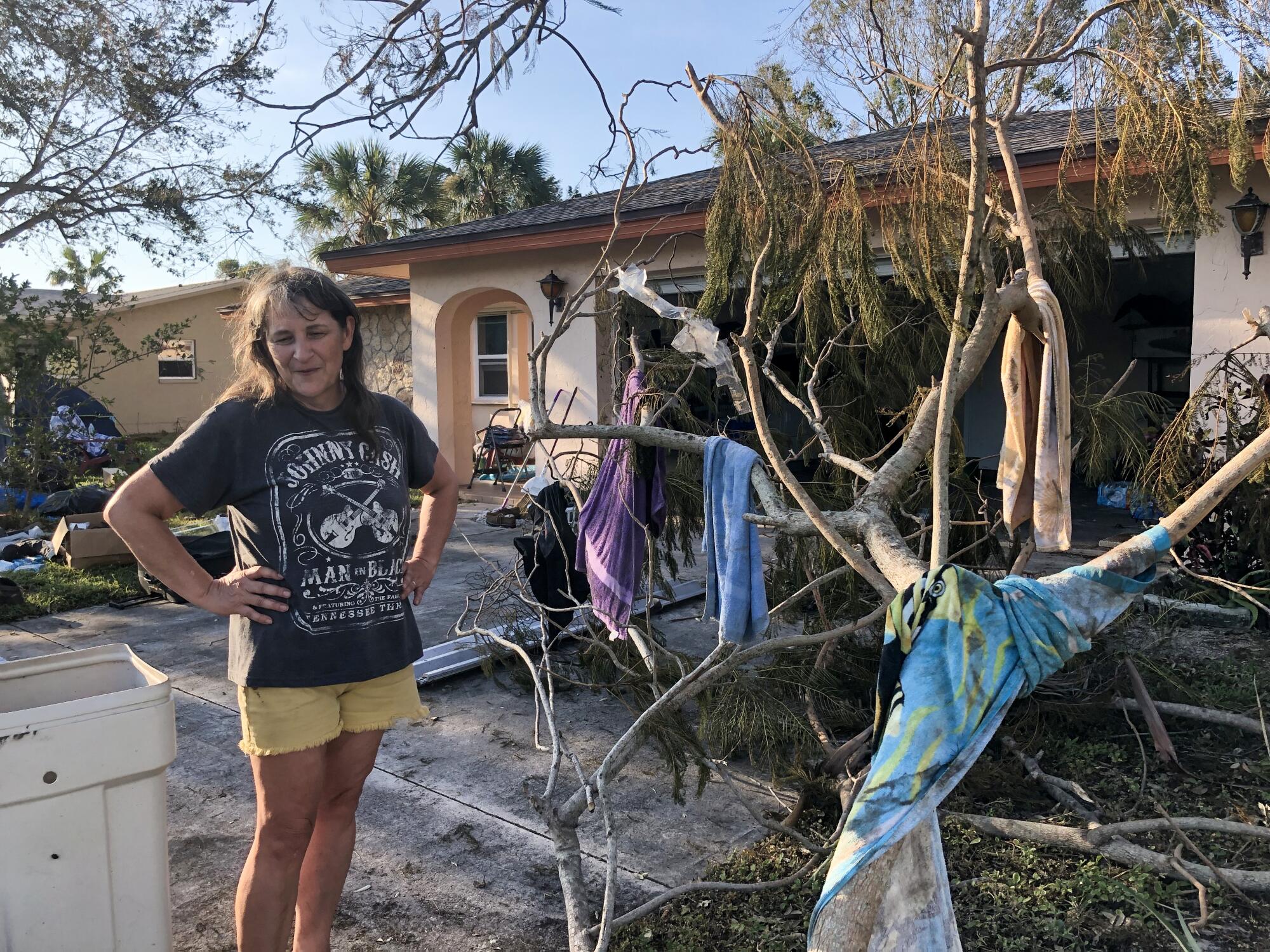 A woman stands in front of a storm-damaged home.
