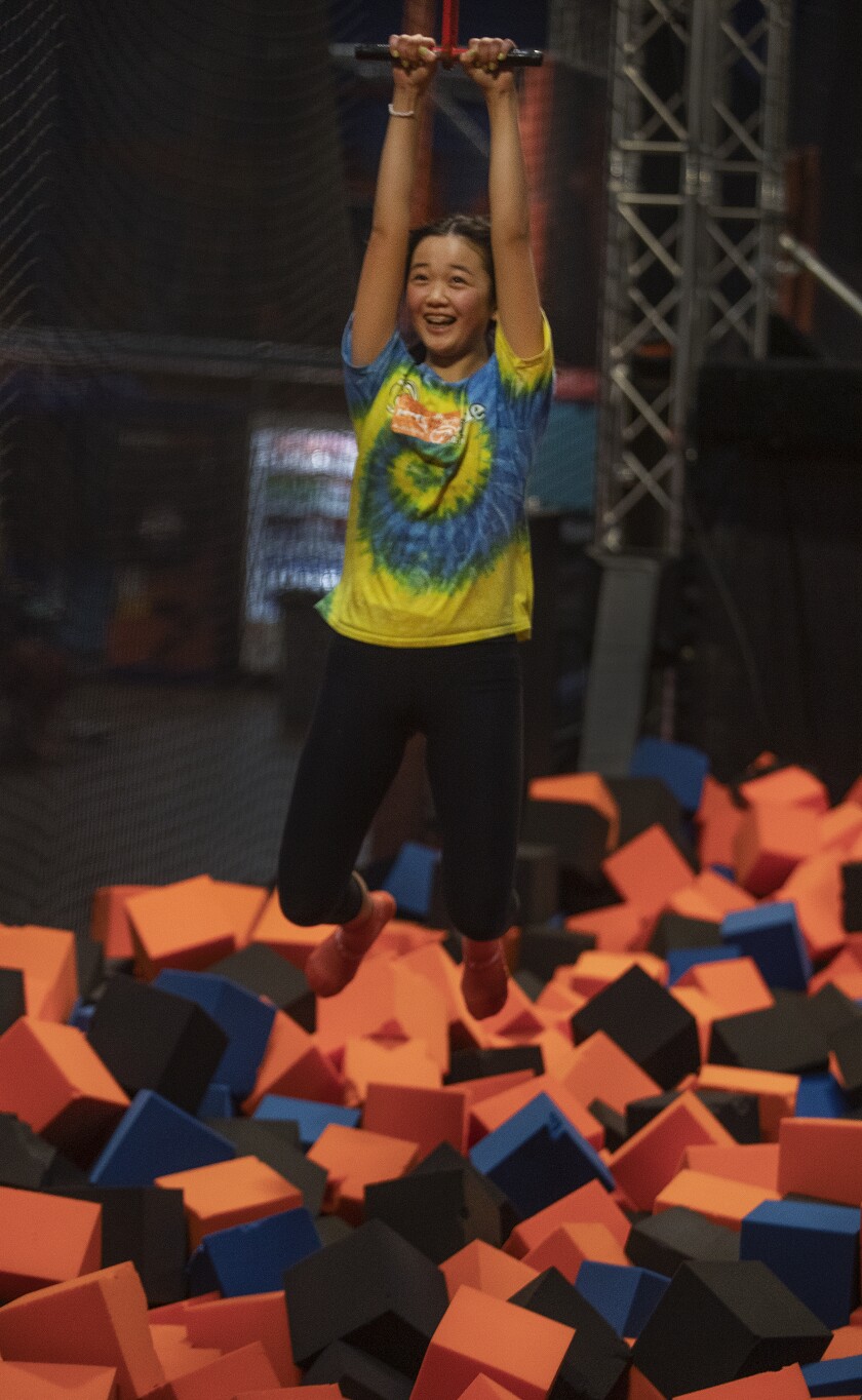 A child rides a zip line above a foam pit.