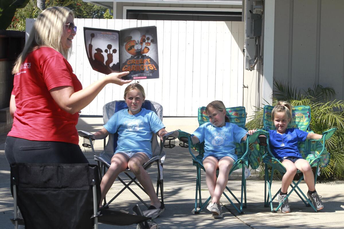 Library Media Technician for Calavara Hills Elementary School Lindsay Rudy reads "Creepy Carrots!" to Hailey Rutledge, 10, left, and her sisters Mia, 8, center, and Kate, 6, while in front of the Rutledge family's home on Friday March 27, 2020 in Carlsbad, California.