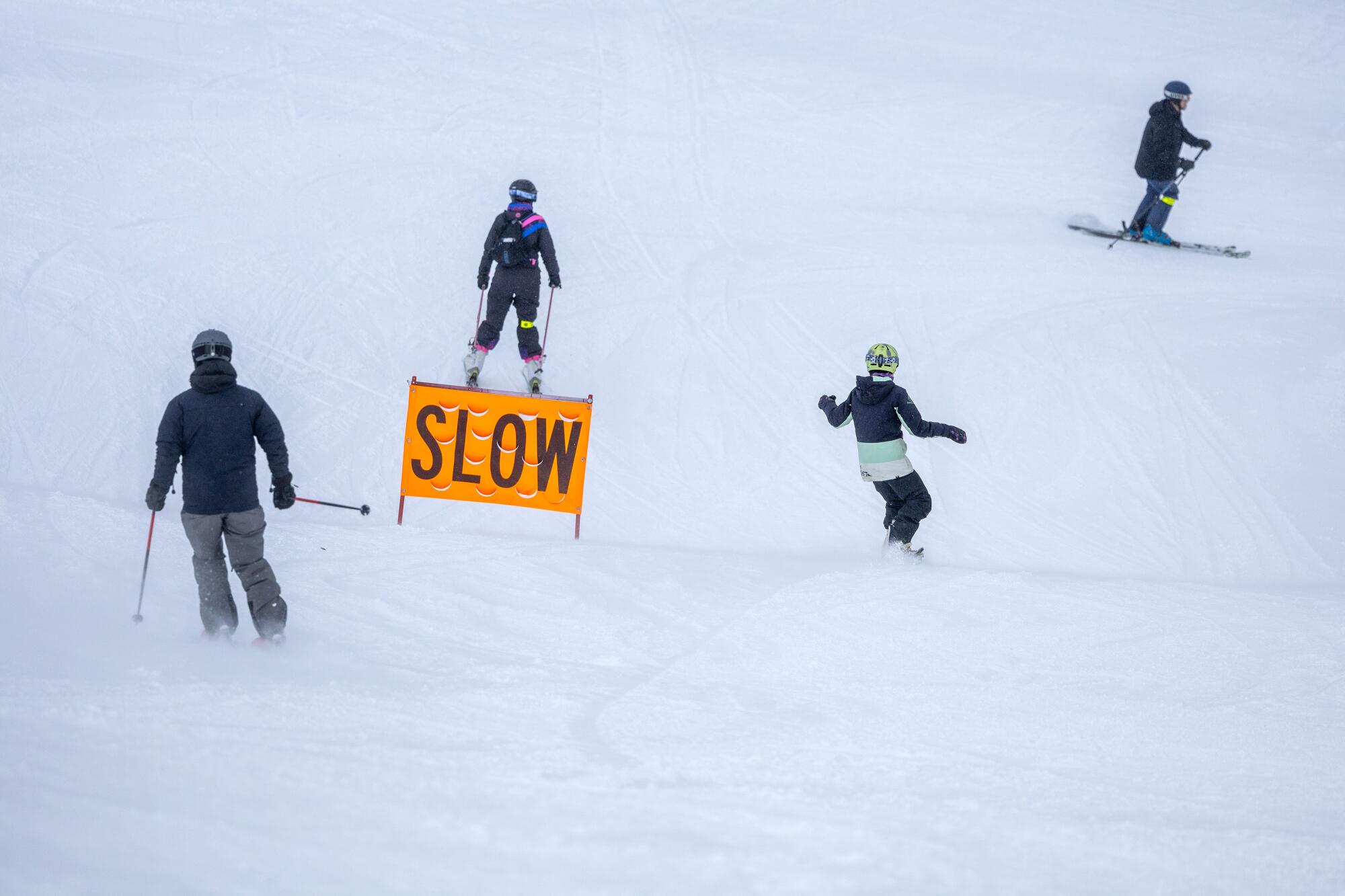 An orange sign on a ski slope warns users to slow down near a trail junction.