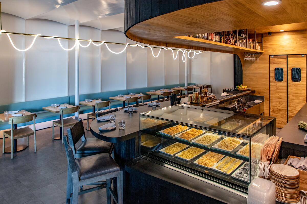 An interior photo of a cocktail bar; in the foreground, a display case of fresh, uncooked pasta sits full.