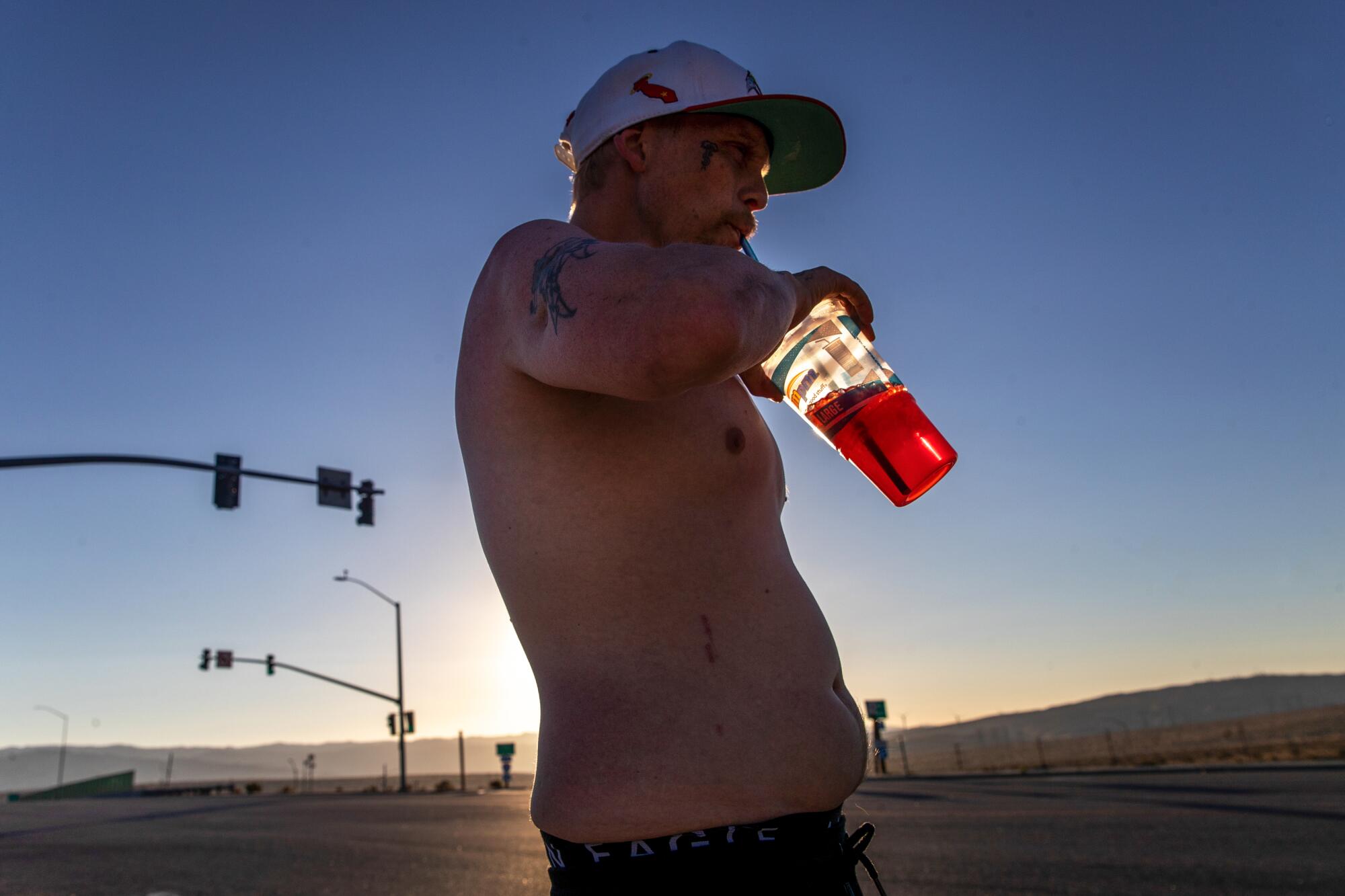 A shirtless man drinks from a plastic cup with a straw.