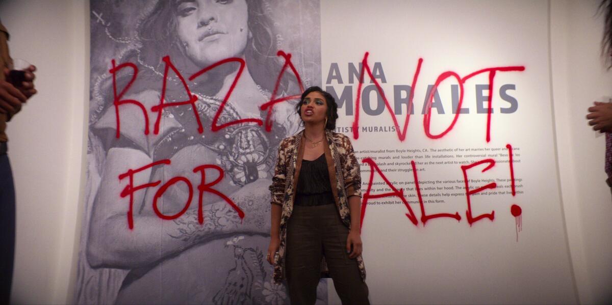 An artist stands before her photo in a gallery, over which is spray-painted "Raza Not for Sale!"