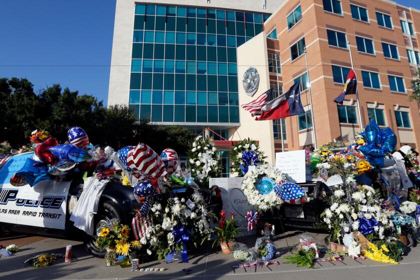 Flower-covered police vehicles sit parked in front of Dallas Police Department headquarters Friday, serving as a makeshift memorial to honor the officers who were killed.