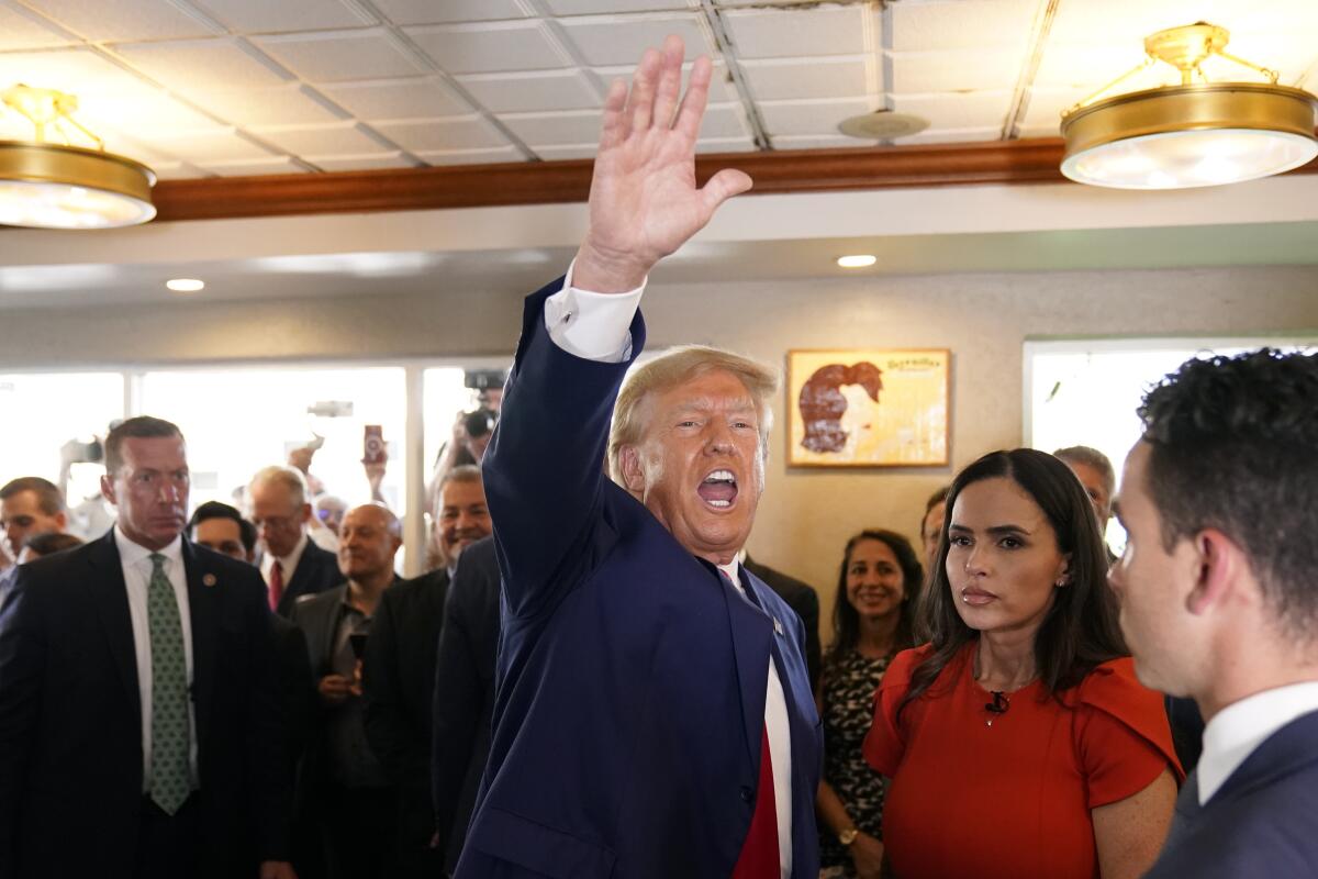 Former President Trump calling and waving to someone out of the frame as he and several other people enter a building.