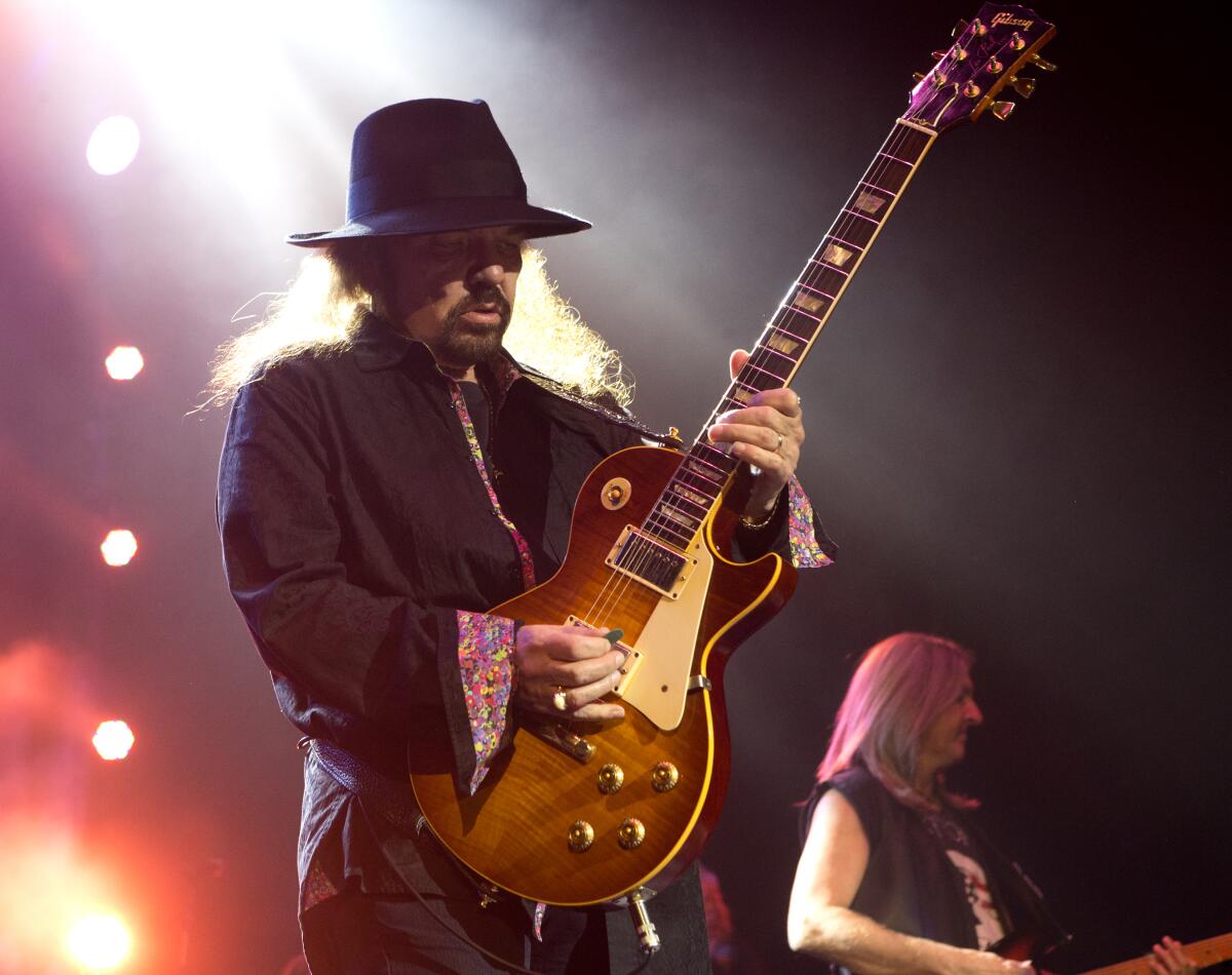 A man with long hair wearing a black fedora and playing the electric guitar on a stage