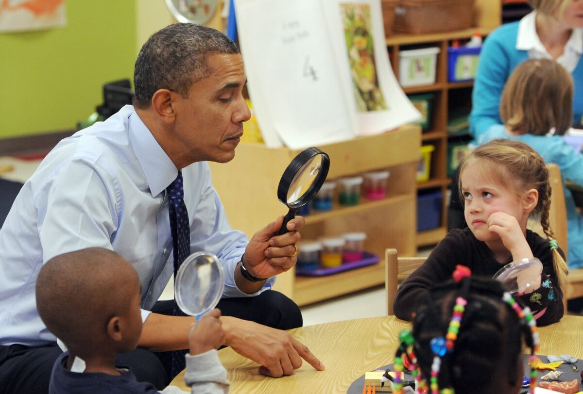 President Obama looks through a spy glass as a little girl stares at him during a visit to College Heights Early Childhood Learning Center in Decatur, Ga.