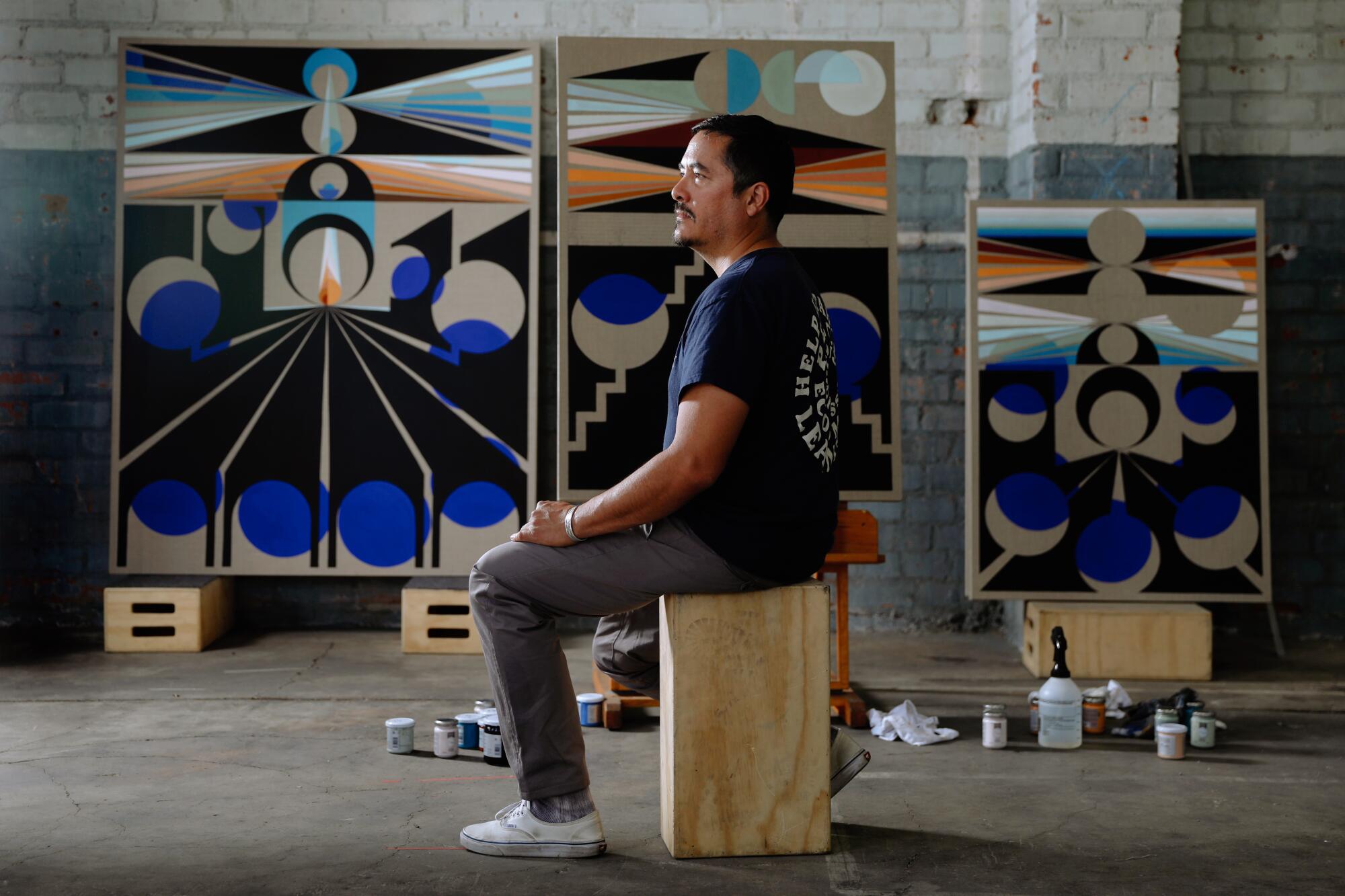 Eamon Ore-Giron is seen sitting on a wooden crate in his studio before a series of works-in-progress