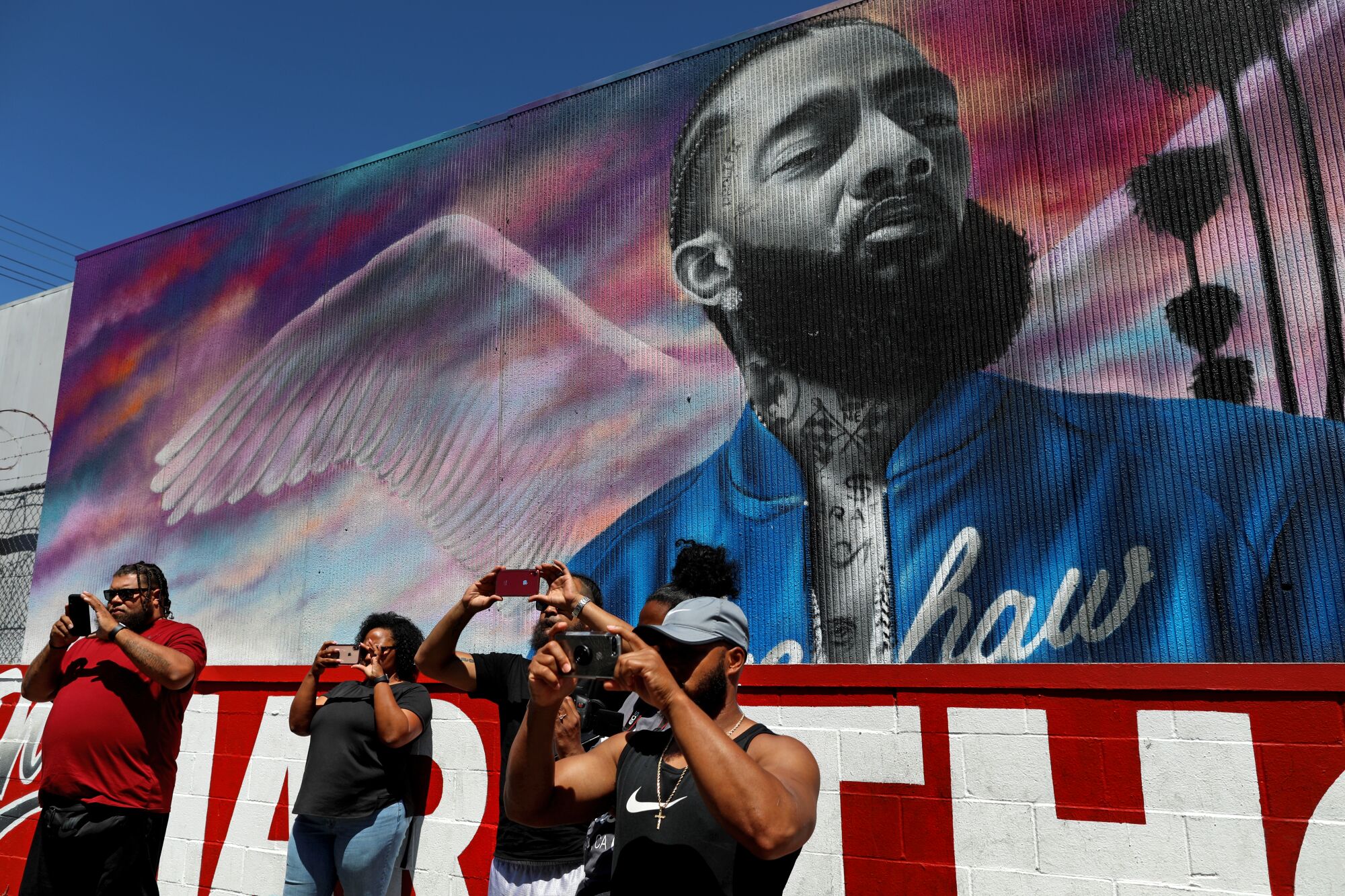 Fans take selfies in front of a mural of Nipsey Hussle