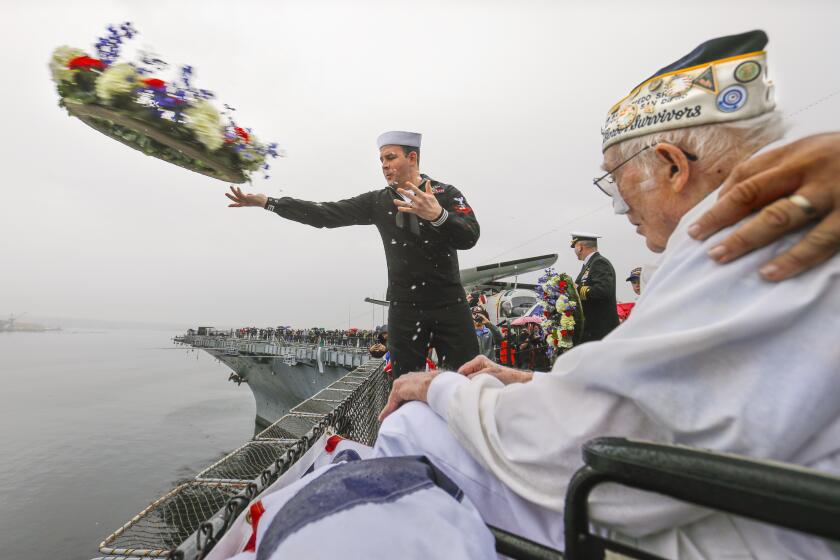 As Clayton Schenkelberg, 102, right, a Navy survivor of the December 7, 1941 attack on Pearl Harbor that pushed America into World War II against Japan, looks on, his great-grandson, Navy Petty Officer 2nd Class Patrick Schenkelberg, left, tosses a memorial wreath into San Diego Bay from the flight deck of the USS Midway Museum during the annual Pearl Harbor Remembrance Ceremony, December 7, 2019 in San Diego, California.