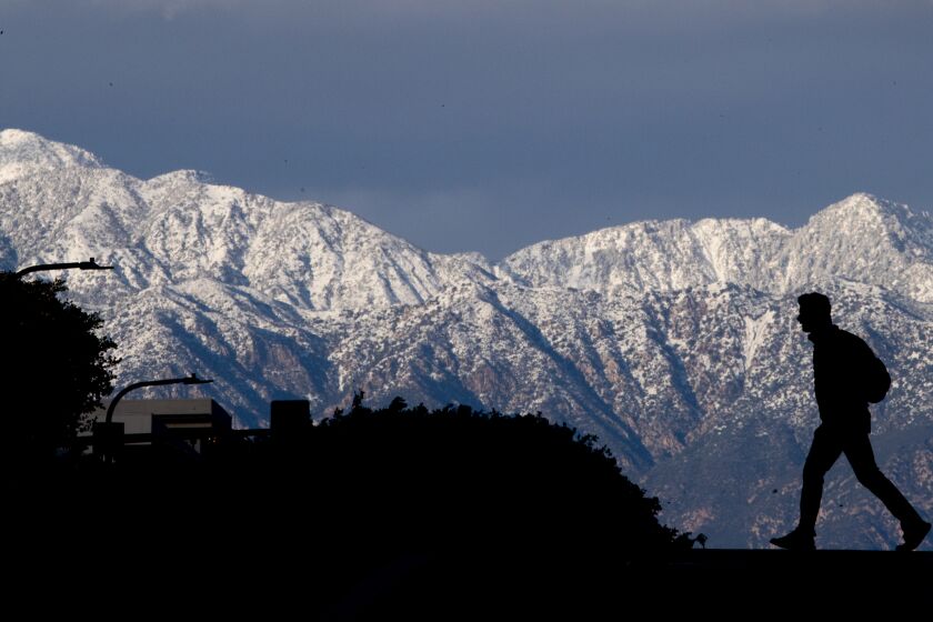 Los Angeles, CA - March 01: A pedestrian crossing the street in downtown Los Angeles is silhouetted against the snow-capped San Gabriel mountains at sunset after historic rain and snow dumped on Southern California in on Wednesday, March 1, 2023 in Los Angeles, CA. (Allen J. Schaben / Los Angeles Times)