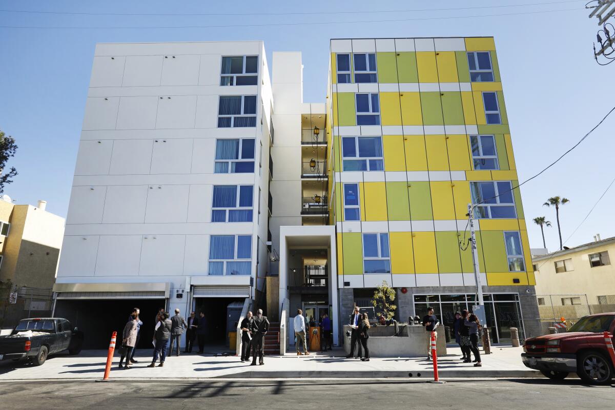 People stand outside a boxy yellow and white housing development