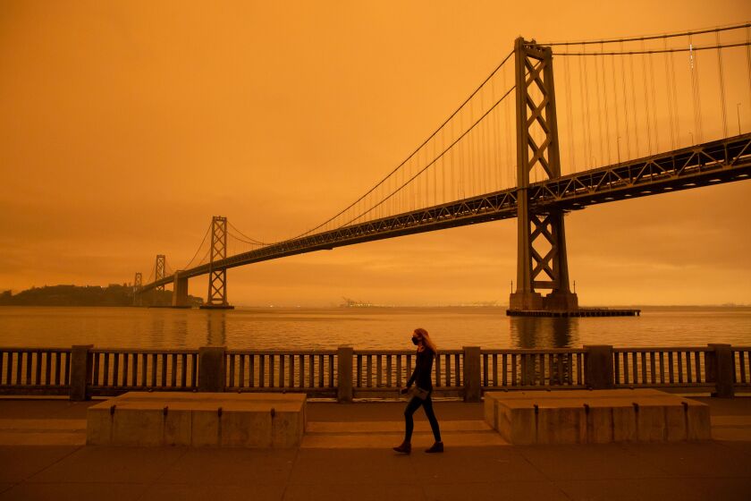 A woman walks along The Embarcadero under an orange smoke-filled sky in San Francisco, California on September 9, 2020. - More than 300,000 acres are burning across the northwestern state including 35 major wildfires, with at least five towns "substantially destroyed" and mass evacuations taking place. (Photo by Brittany Hosea-Small / AFP) (Photo by BRITTANY HOSEA-SMALL/AFP via Getty Images)