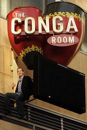 Brad Gluckstein, founder and co-owner of the new Conga Room, perches on the club's sign. The Conga Room, which used to be in the Miracle Mile neighborhood, will reopen next to the Nokia Theatre, across the street from Staples Center.