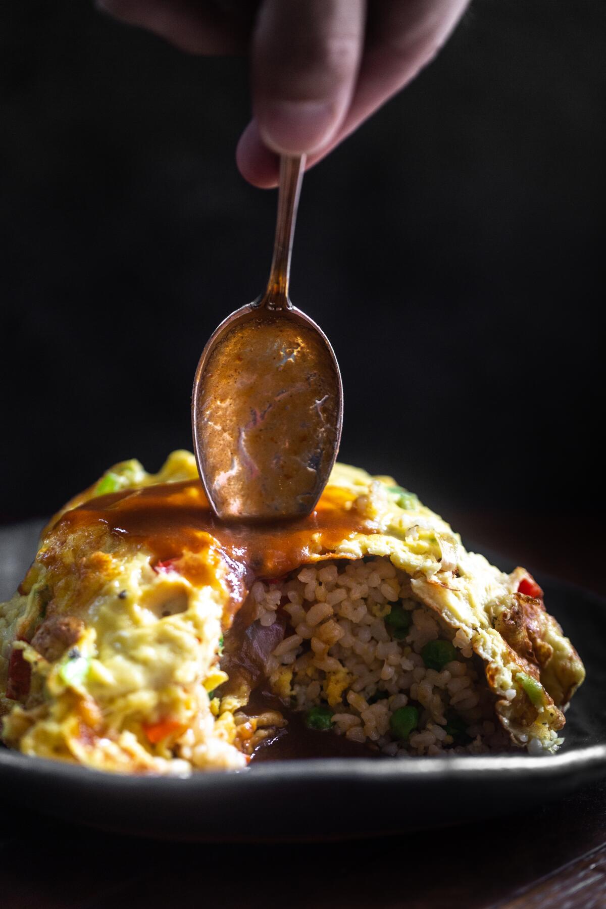 A spoon is poised to dig into a heap of omurice, or omelet rice.