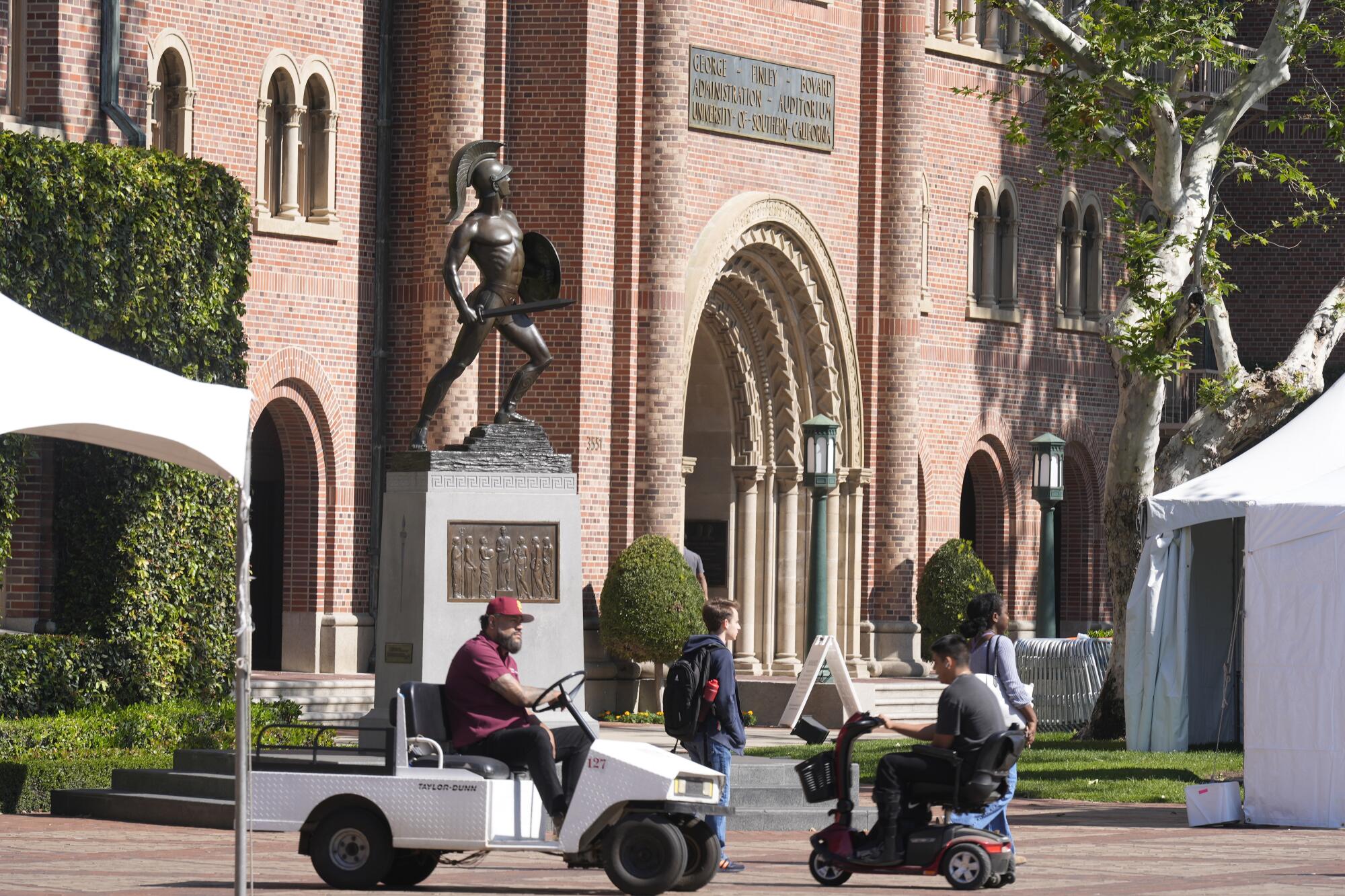 People in vehicles pass the Tommy Trojan statue.