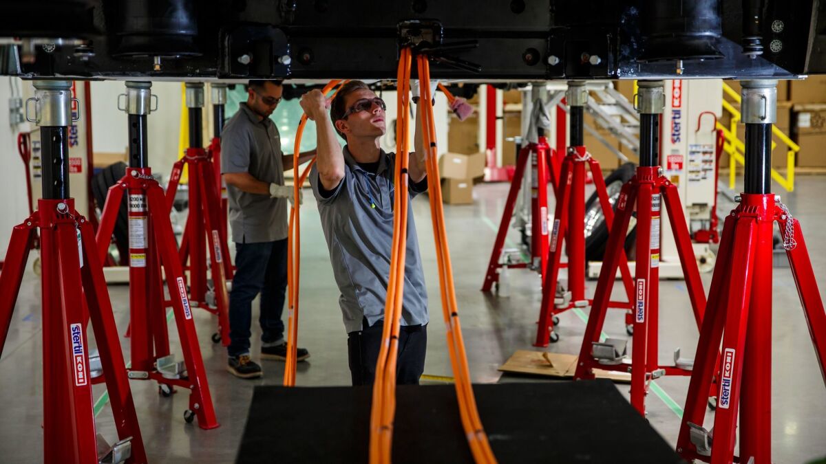 Workers line up cables under an electric bus. (Marcus Yam / Los Angeles Times)