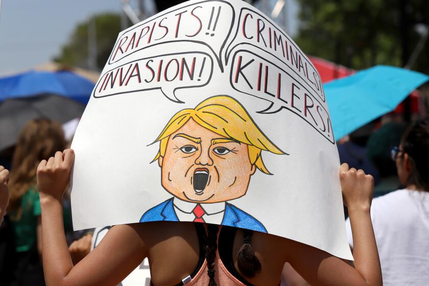 A protester sheilds herself from the sun with a sign at a protest rally during President Trump’s visit to El Paso, TX. Wednesday.