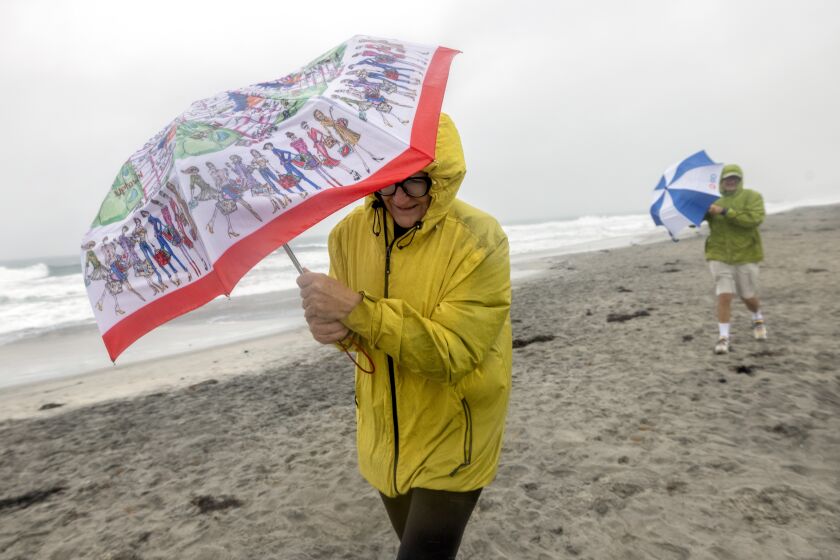 ENCINITAS, CA - DECEMBER 11, 2022: Vera and Konstantin Okun brave wind and rain to do their daily beach walk at Cardiff State Beach in Encinitas as a Pacific storm hits San Diego County on Sunday, December 11, 2022. (Hayne Palmour IV / For The San Diego Union-Tribune)