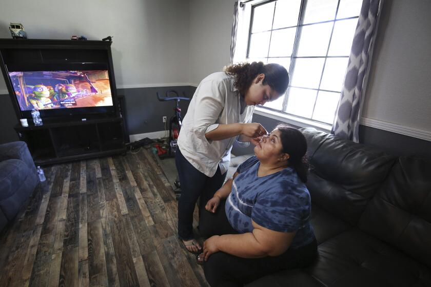 Marvin Estela Pineda (derecha), natural de El Salvador, que se quedó ciega por un glaucoma, espera mientras su hija Mayde le suministra unas gotas, en Madera, California, el 30 de mayo de 2024. (AP Foto/Gary Kazanjian)