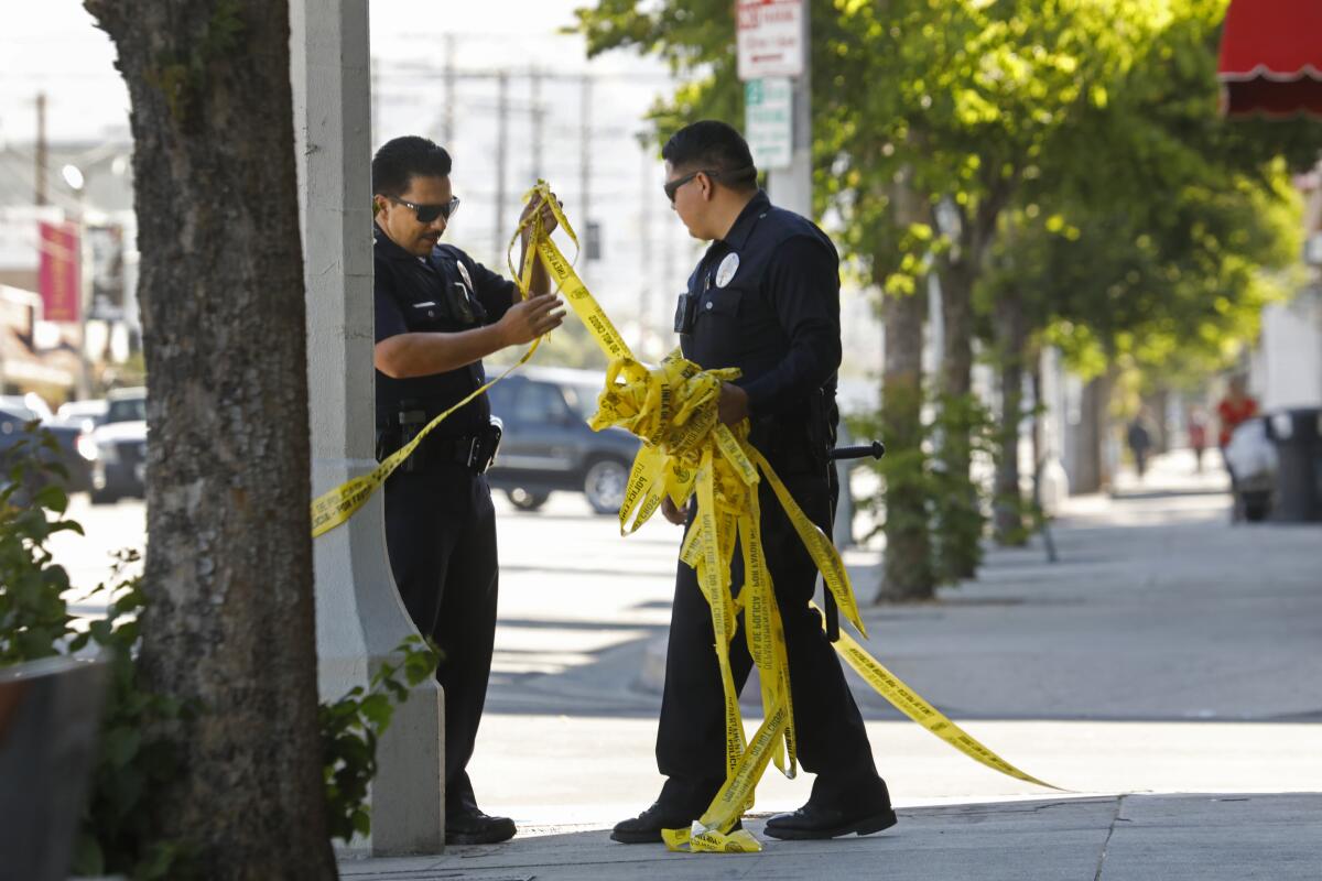 Police remove yellow crime scene tape from a sidewalk