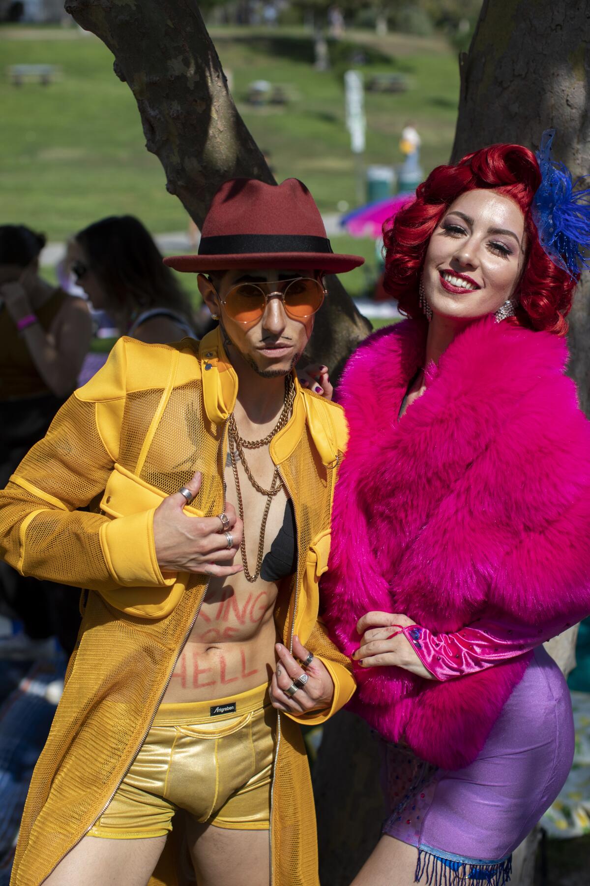 A person in a yellow jacket and boxers and brown cowboy hat, next to a person in purple spandex skirt and pink furry jacket