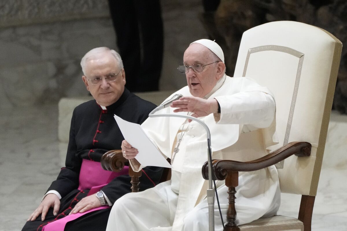 Pope Francis gestures as he speaks from a chair into a microphone