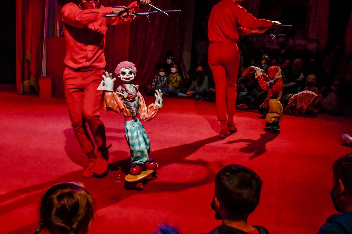 Children seated on the floor watch a performer manipulate a clown marionette puppet.