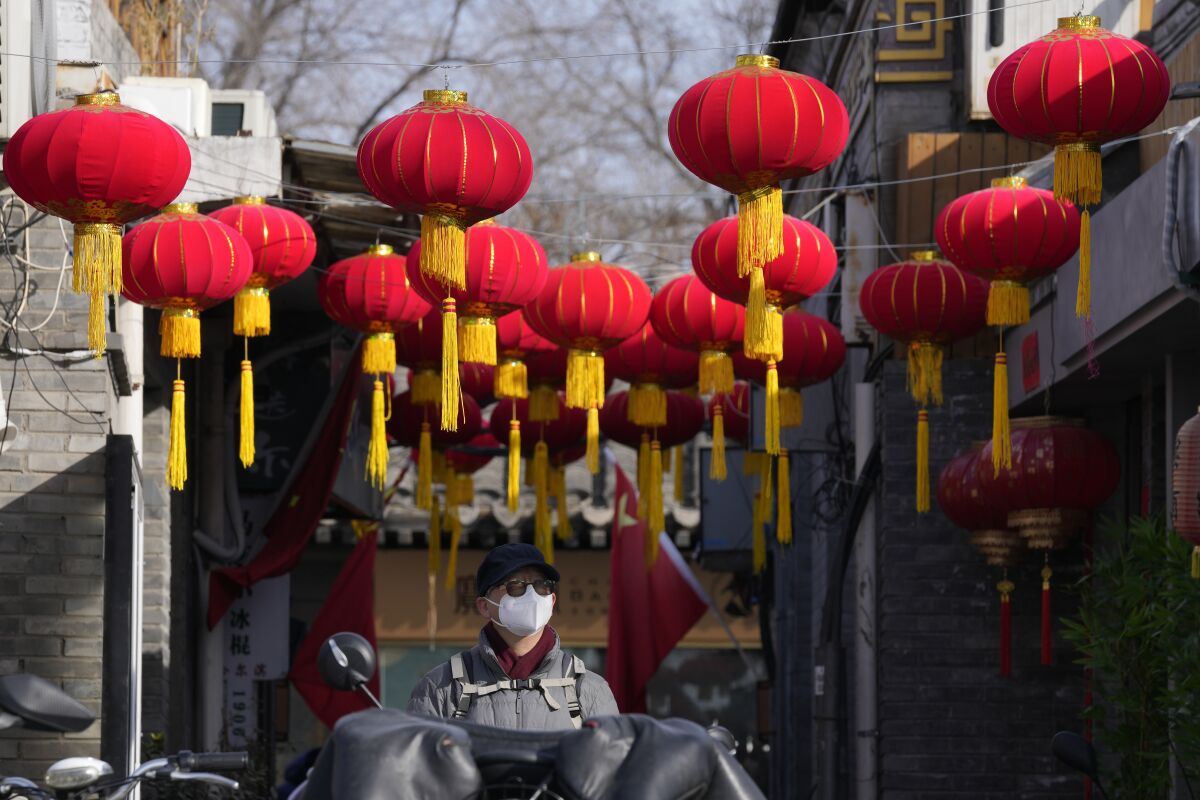 A resident wearing a face mask walks under red lanterns setup for the Lunar New Year holidays in Beijing, China, Monday, Feb. 7, 2022. As China gets back to business after a muted Chinese New Year holiday that coincided with the start of the pandemic-restricted Beijing Olympic Winter Games, the feeling inside and out of the bubble in this auspicious Year of the Tiger is that festivities for the most sacred and important holiday for the country were limited and underwhelming. (AP Photo/Ng Han Guan)